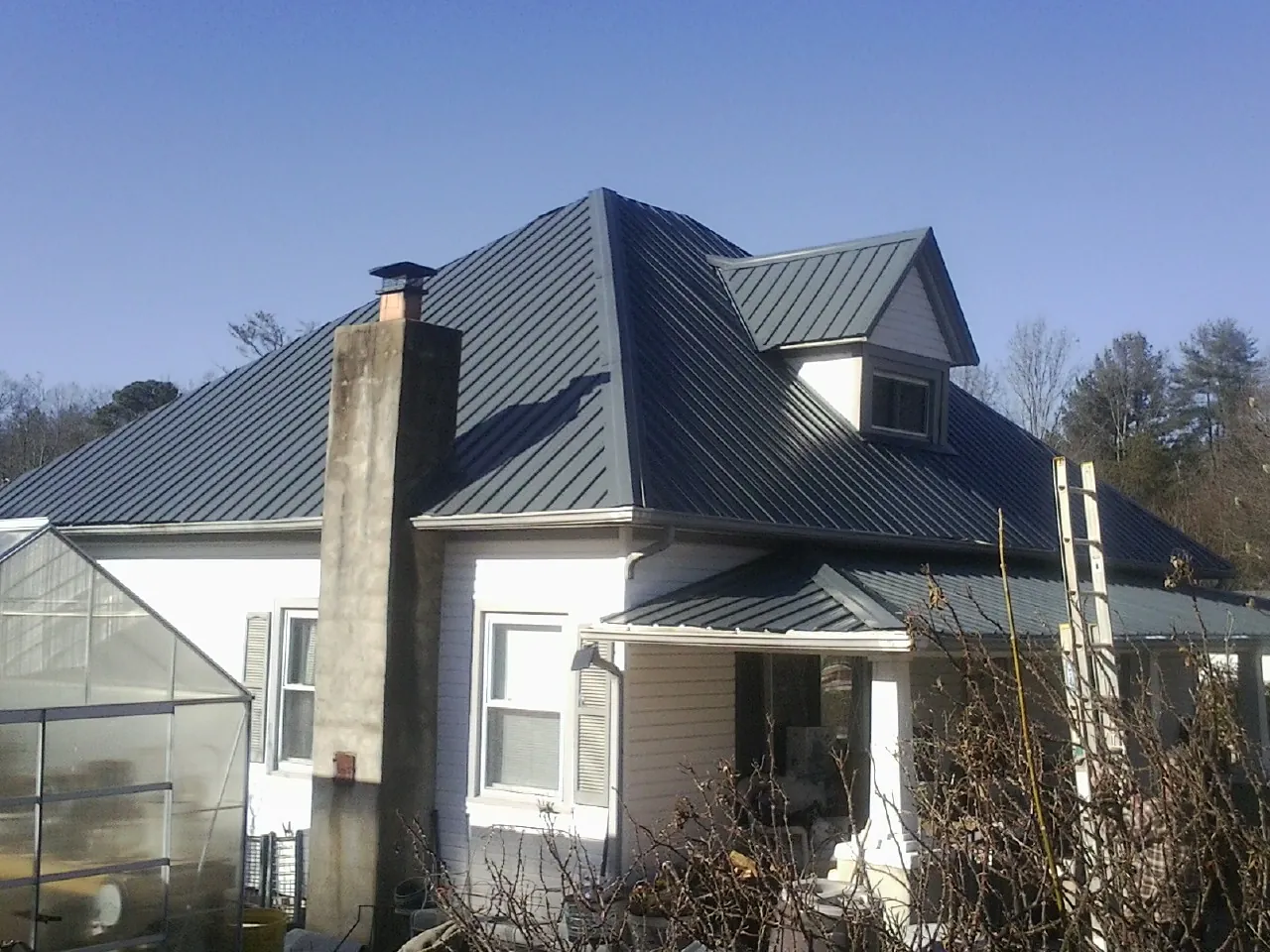 Dark blue standing seam metal roof on a white farmhouse with dormer — Slate & Tile Roof Repair by Roofing Brothers in Chula