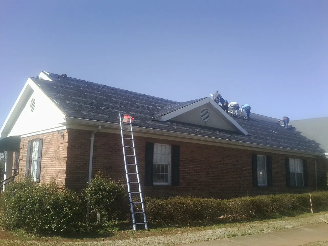 Crew tearing shingles off a brick ranch roof with a ladder set — Metal Roof Repair work by our crew in Chula