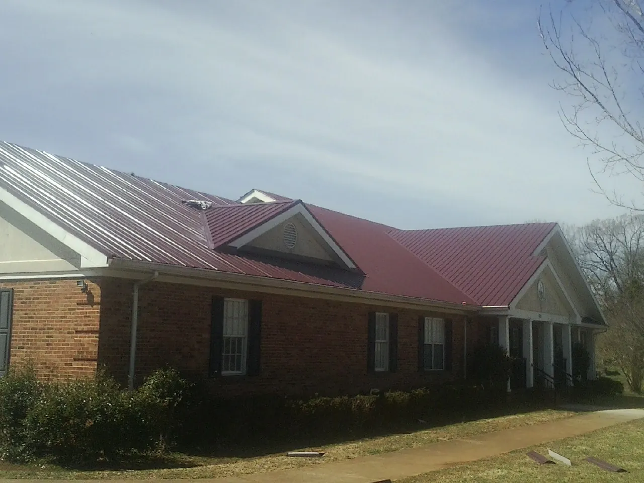 Red metal roof with gabled entries on a long brick building, from a Hail Damage Roof Repair job in Chula