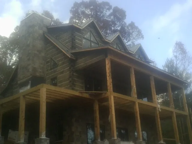 Stone chimney and dormers on a large log home with a timber porch in Chula
