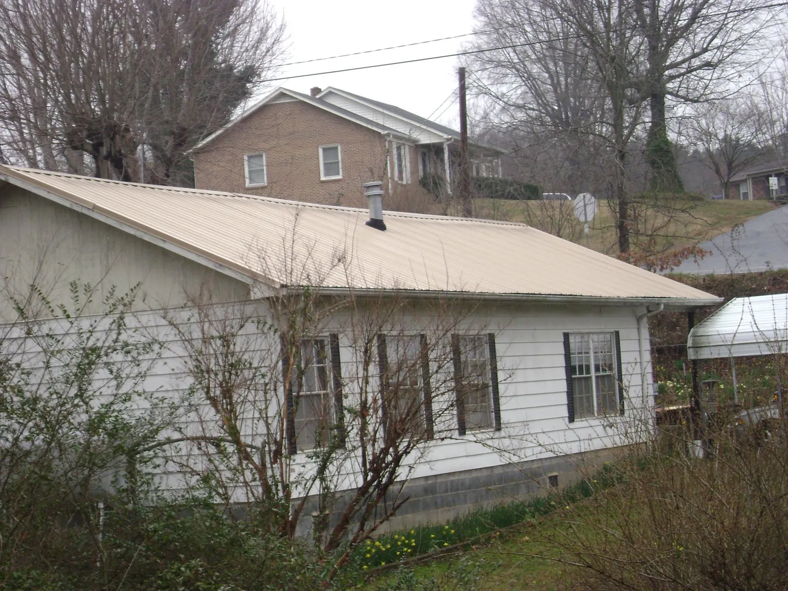 Tan metal roof on a white sided house set into a hillside — Commercial Roofing by Roofing Brothers in Chula
